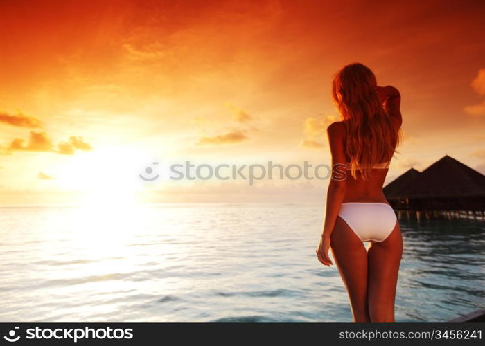 woman in a dress on a bridge home sea and the maldivian sunset on the background