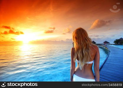 woman in a dress on a bridge home sea and the maldivian sunset on the background