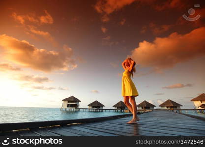 woman in a dress on a bridge home sea and the maldivian sunset on the background