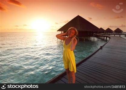 woman in a dress on a bridge home sea and the maldivian sunset on the background