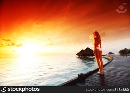 woman in a dress on a bridge home sea and the maldivian sunset on the background