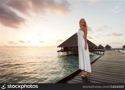 woman in a dress on a bridge home sea and the maldivian sunset on the background