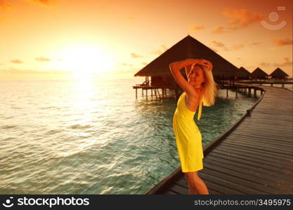 woman in a dress on a bridge home sea and the maldivian sunset on the background