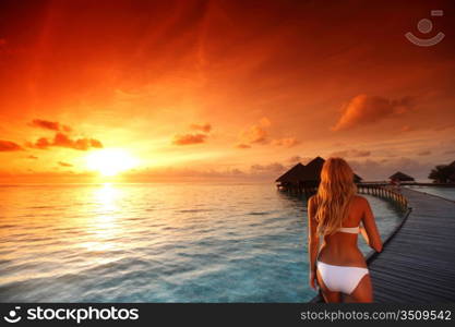 woman in a dress on a bridge home sea and the maldivian sunset on the background