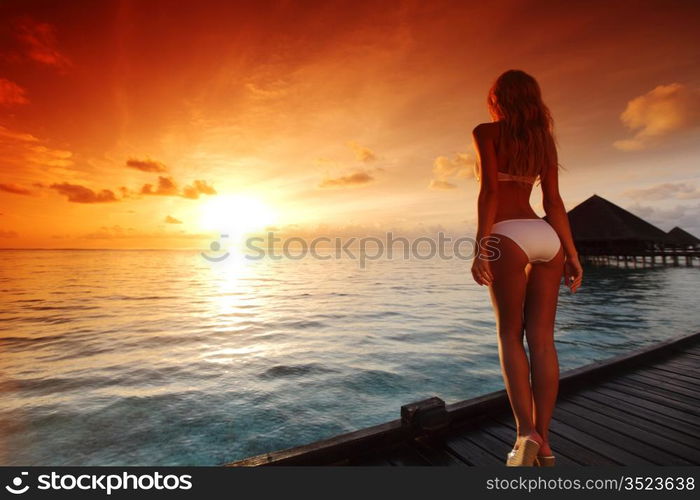 woman in a dress on a bridge home sea and the maldivian sunset on the background