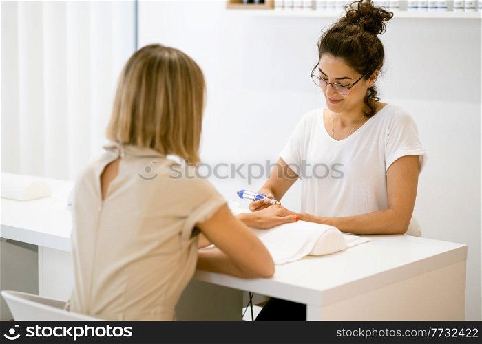 Woman in a nail salon receiving a manicure by a beautician with. Beautician file nails to a customer.. Woman in a nail salon receiving a manicure by a beautician with.