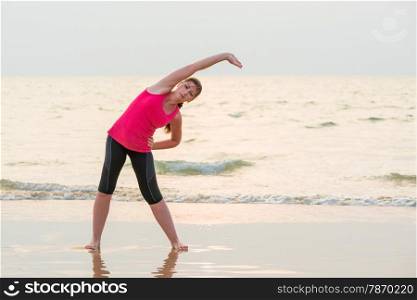 woman in a pink shirt doing exercises on the wet sand