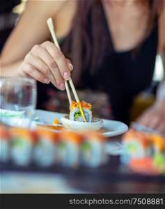 Woman in a restaurant dines sushi, dips a slice of a rolls in soy sauce, trendy Asian food, a tasty oriental cuisine