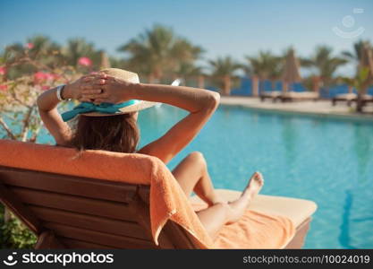 Woman in a straw hat relaxing on a daybed near a luxurious summer pool hotel Egypt, concept time to travel.. Woman in a straw hat relaxing on a daybed near a luxurious summer pool hotel Egypt, concept time to travel