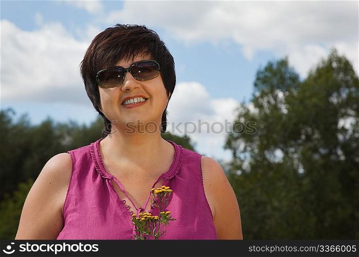 woman in a sunny day on a wood clearing smiles and holds flowers, in sunglasses
