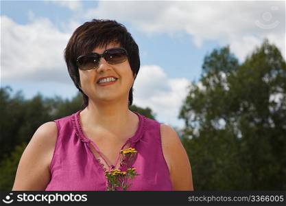 woman in a sunny day on a wood clearing smiles and holds flowers, in sunglasses
