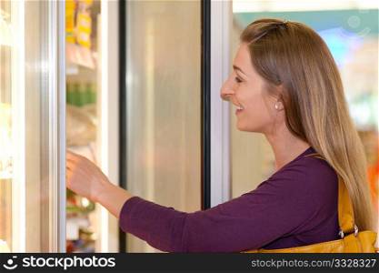 Woman in a supermarket standing in front of the freezer looking for her favorite frozen food