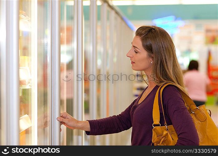 Woman in a supermarket standing in front of the freezer looking for her favorite frozen food