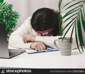 woman in a sweater sleeps at a work table, next to a laptop. Fatigue and overwork concept. Laziness
