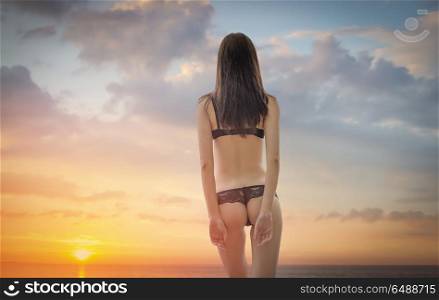 woman in a swimsuit is standing ass at sunset. woman in a swimsuit is standing ass