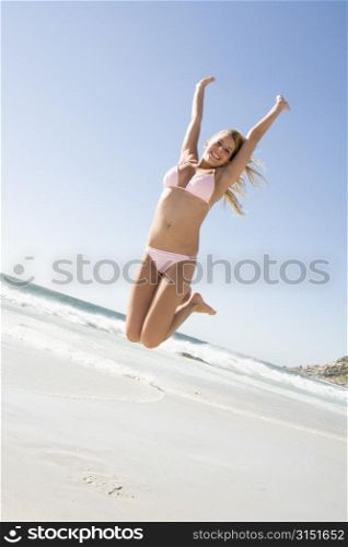 Woman in a two piece bathing suit jumping on a beach