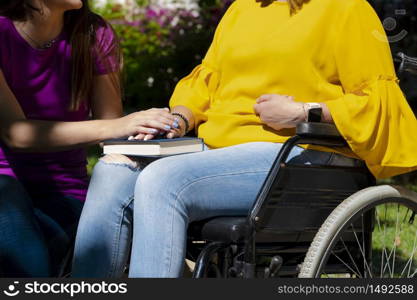 Woman in a wheelchair holding hands with her young daughter on her lap on an out of focus background. Disability and family concept.. Woman in a wheelchair holding hands with her young daughter on her lap