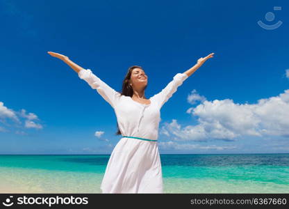 Woman in a white dress on beach. Woman in a white dress is walking on the blue sea beach background with hands raised