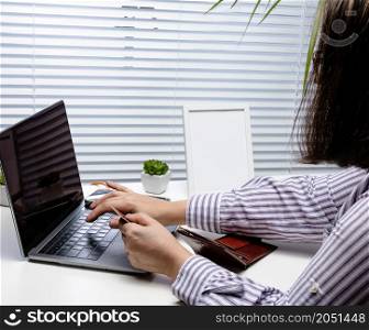 woman in a white striped shirt makes purchases online with a laptop, a credit card in hand. A woman sitting at a white table