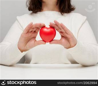woman in a white sweater holding a red heart, the concept of love and kindness. Donation