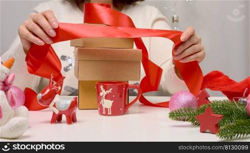 woman in a white sweater sits at the table and wraps gifts for Christmas. Preparing for the holidays