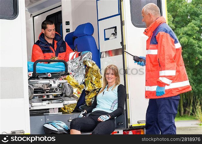 Woman in ambulance with emergency paramedics aid bike accident smiling