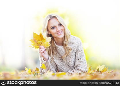 Woman in autumn park. Happy woman lies on dry leaves in autumn park at sunny day