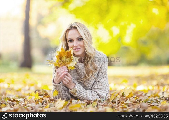 Woman in autumn park. Happy woman lies on dry leaves in autumn park at sunny day