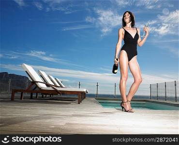 Woman in bathing suit standing with champagne at outdoor pool