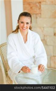 Woman in bathrobe having morning coffee on terrace