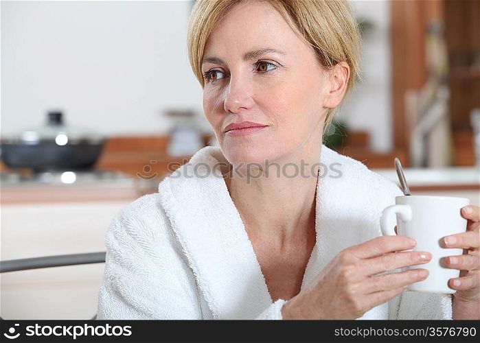 Woman in bathrobe sat in kitchen