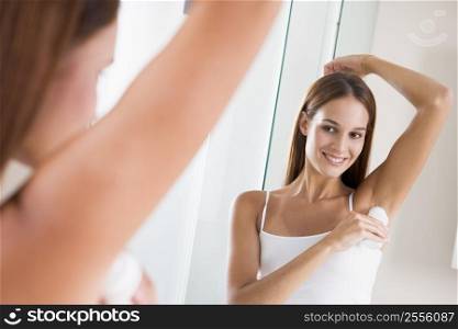 Woman in bathroom applying deodorant and smiling