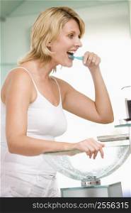 Woman in bathroom brushing teeth and smiling