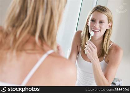 Woman in bathroom brushing teeth smiling