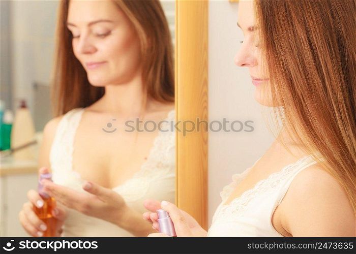 Woman in bathroom holding bottle with cosmetic oil. Girl taking care of her long smooth hair applying cream cosmetics. Haircare concept.. Woman taking care of her long hair applying cosmetic oil
