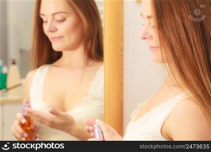 Woman in bathroom holding bottle with cosmetic oil. Girl taking care of her long smooth hair applying cream cosmetics. Haircare concept.. Woman taking care of her long hair applying cosmetic oil