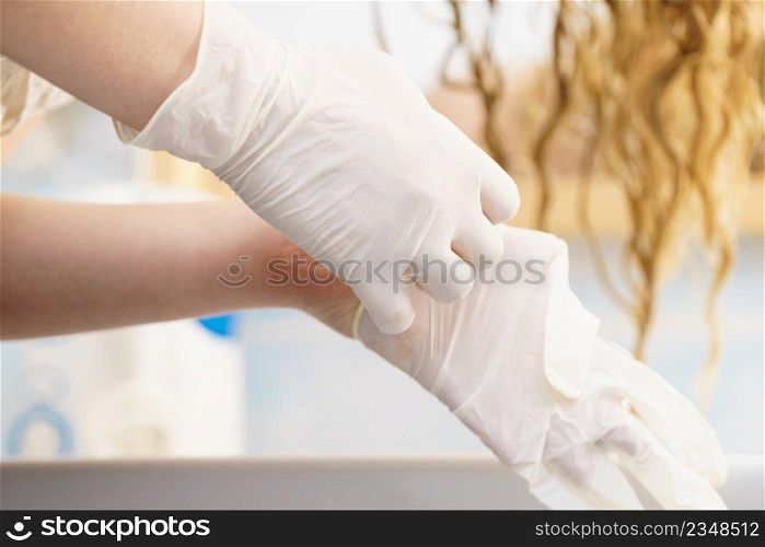Woman in bathroom putting on white latex protective gloves before hair dyeing.. Woman with white latex gloves in bathroom
