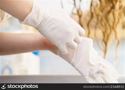 Woman in bathroom putting on white latex protective gloves before hair dyeing.. Woman with white latex gloves in bathroom