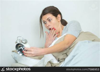 woman in bed looking in shock at alarm clock