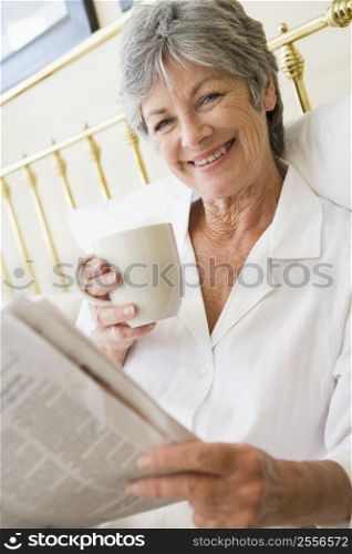 Woman in bedroom with coffee and newspaper smiling