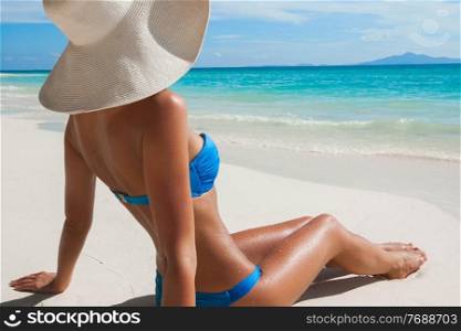 Woman in big sun hat sitting on beach by the sea side view. Woman in sun hat sitting on beach