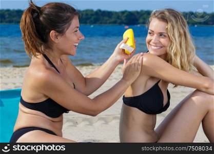 woman in bikini applying sun block cream on friend