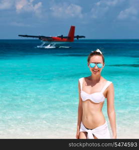 Woman in bikini at tropical beach. Seaplane at background.