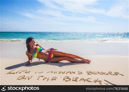 Woman in bikini lies on sea beach , Life is always better on the beach, conceptual handwriting on sand. Woman lies on sea beach