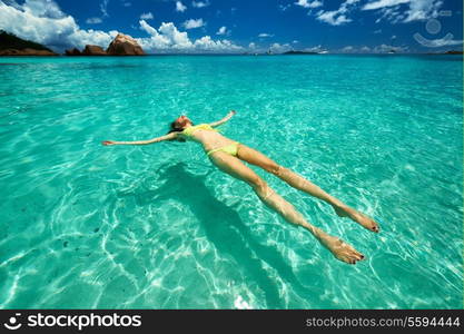 Woman in bikini lying on water at tropical beach