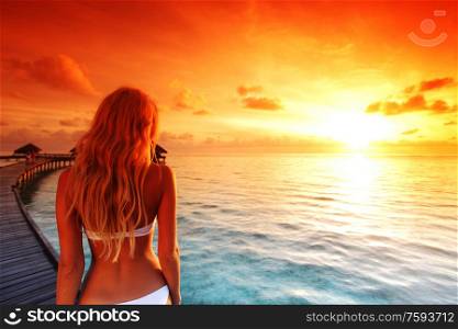 woman in bikini on a bridge home sea and the maldivian sunset on the background. woman in bikini on maldivian sunset