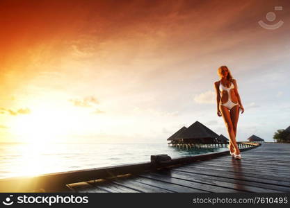 woman in bikini on a bridge home sea and the maldivian sunset on the background. woman in bikini on maldivian sunset