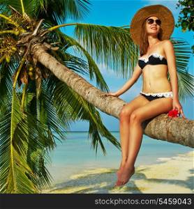 Woman in bikini sitting on a palm tree at tropical beach, Maldives