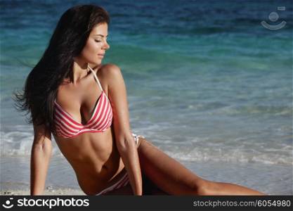 Woman in bikini sitting on beach. Beautiful young woman in bikini sitting on beach near sea