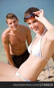 Woman in bikini sunbathing by sea on beach, man in background